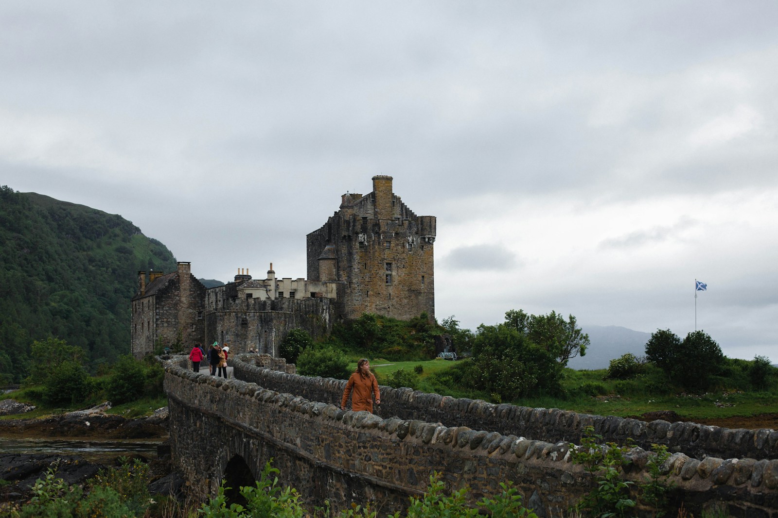 People walking on a bridge toward Eilean Donan Castle in Scotland.